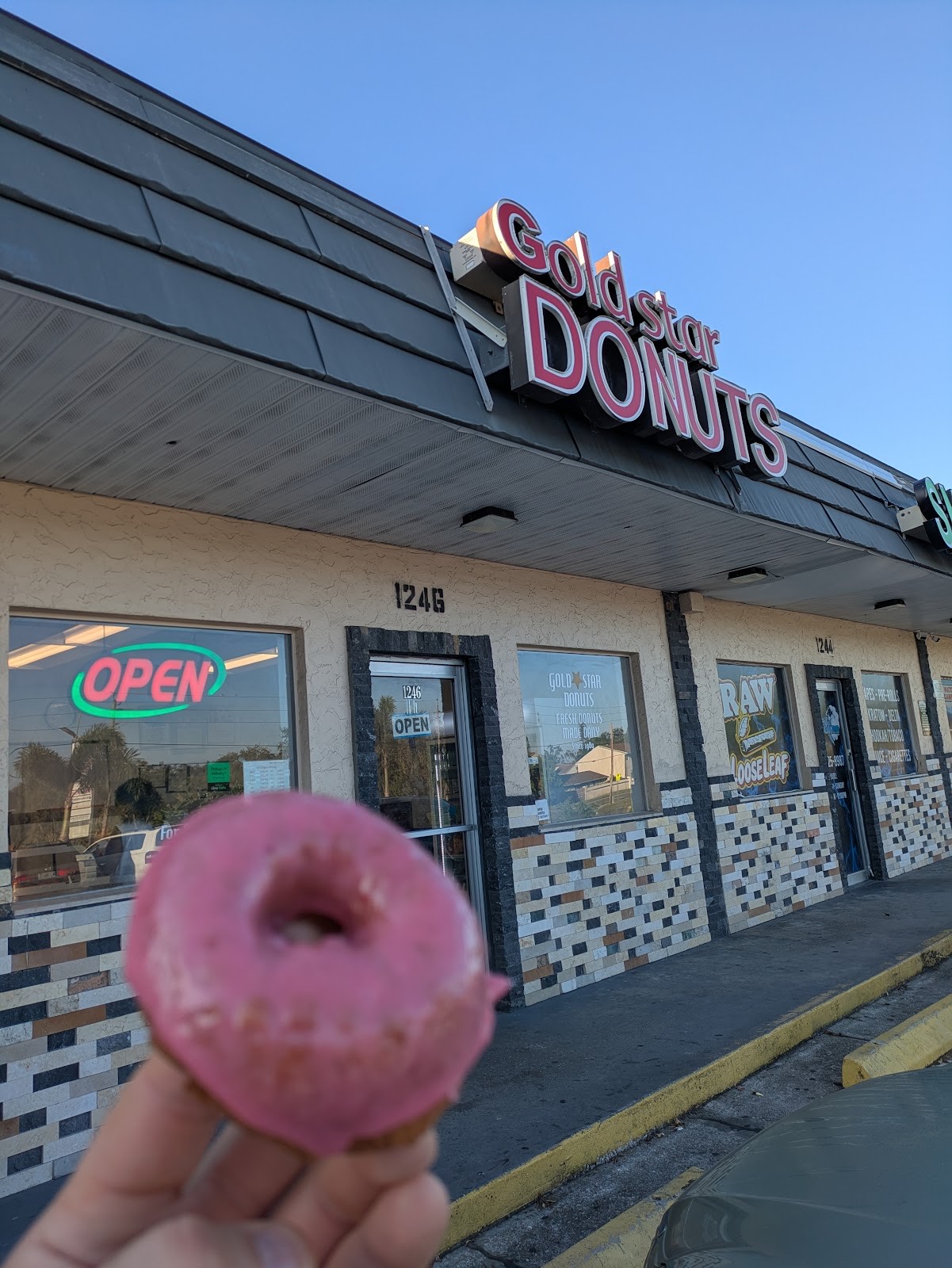 The Gold Star Donuts storefront with its red sign and a strawberry-glazed donut held in front