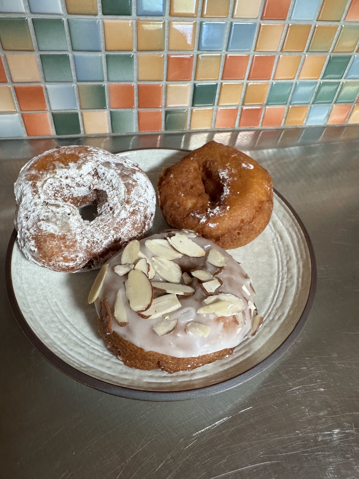 Powdered, plain old-fashioned and almond-glazed donuts on a plate against a colorful retro tile wall