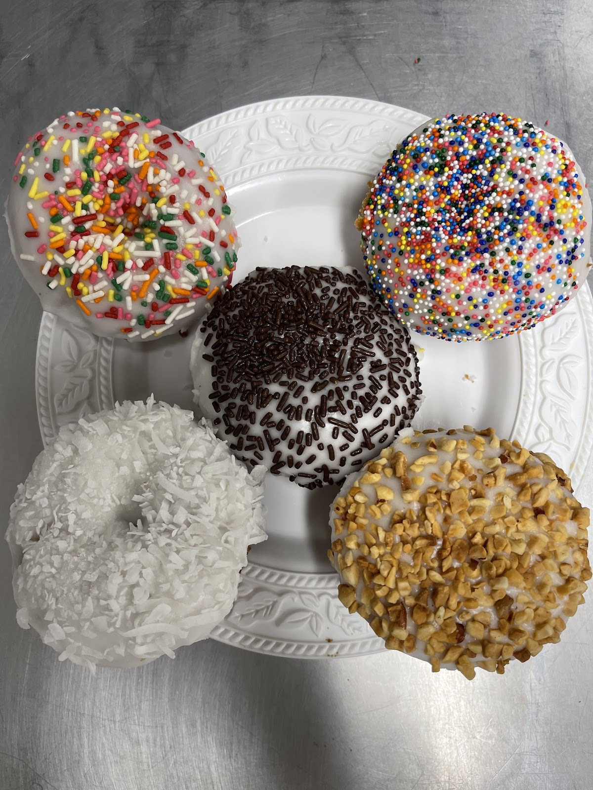 Assorted iced donuts with rainbow and chocolate sprinkles, coconut and nuts on white plates